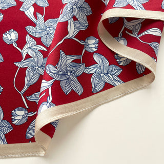 Close-up of a silk bandana scarf by LuluLane with vibrant red background featuring blue floral botanical pattern and cream-colored border.