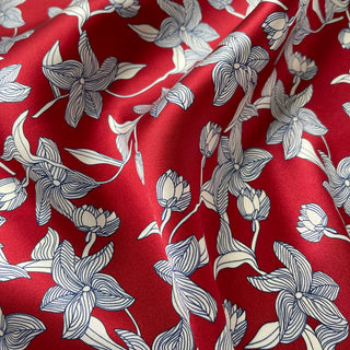 Close-up of women's silk bandana scarf by LuluLane with vibrant red background featuring blue floral botanical pattern.