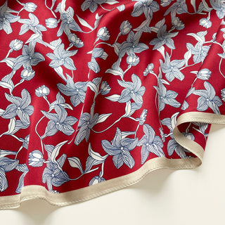 Close-up of a silk bandana scarf by LuluLane with vibrant red background featuring blue floral botanical pattern and cream-colored border.