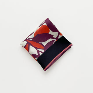 Folded silk bandana scarf by LuluLane with burgundy background, cream white floral print, and orangey red leaves, framed by black border with hand-rolled edges.