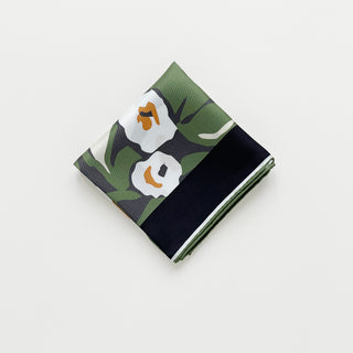 Folded silk bandana scarf by LuluLane with green background, cream white floral print, and yellow leaves, framed by black border with hand-rolled edges.