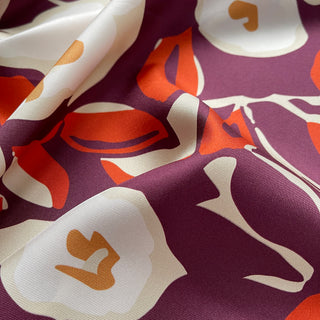 Close-up of a silk bandana scarf by LuluLane with burgundy background, cream white floral print, and orangey red leaves.