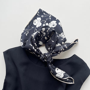 a black and white rose print silk scarf with hand-rolled edges, knotted as a neck scarf, paired with a black dress