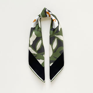 Silk bandana scarf by LuluLane with green background, cream white floral print, and yellow leaves, framed by black border with hand-rolled edges.