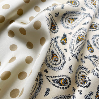 Close-up of beige silk scarf by LuluLane with intricate black paisley pattern on one side, solid cream color on the other, featuring elegant brown border trim