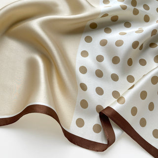 Close-up of Beige silk scarf by LuluLane with polka dot pattern on one side, solid cream colour on the other, featuring elegant brown border trim