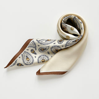 Beige silk scarf by LuluLane with intricate black paisley pattern on one side, solid cream colour on the other, featuring elegant brown border trim