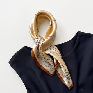 Pale apricot silk bandana scarf with elegant black line art designs and copper-brown border, elegantly draped on navy blue fabric