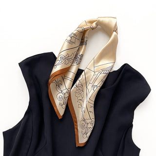 Pale apricot silk bandana scarf with black architectural line drawings and copper border, elegantly draped on a navy garment