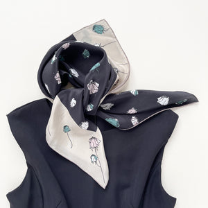a luxury floral rose black silk scarf with beige edge, featuring hand-rolled hems, tied as a neck scarf, paired with a sleeveless black dress  