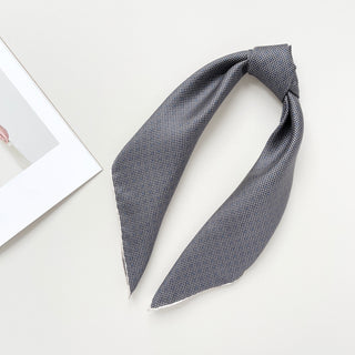 Folded black and white silk scarf with classic grid and dot pattern displayed on white background, showing luxurious sheen and hand-rolled edges