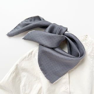 Blue and white silk bandana with grid pattern and dots, styled around collar of white shirt, showing sheen and texture of luxurious fabric