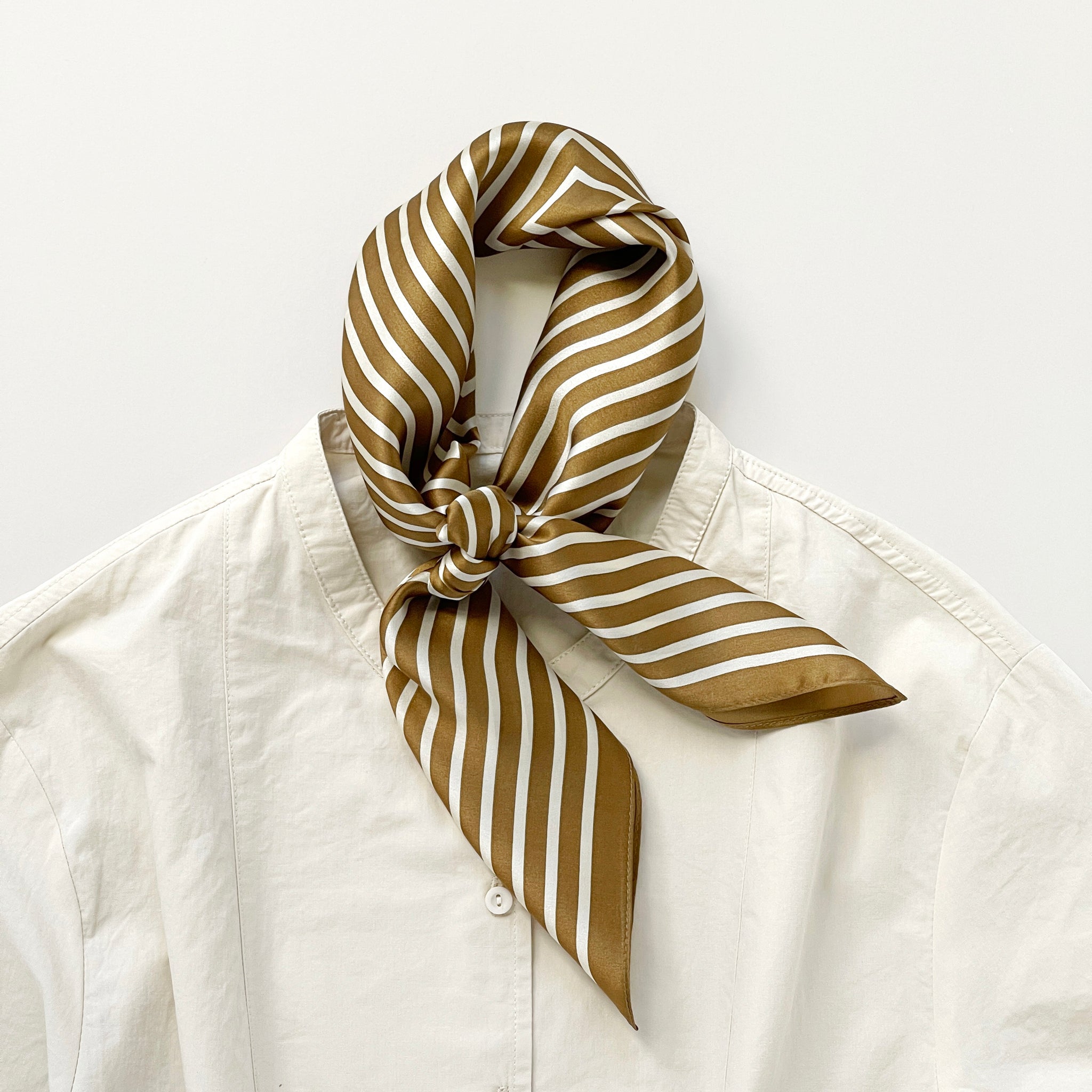 a striped silk scarf in bronze knotted as a neck scarf, paired with a light being women's blouse