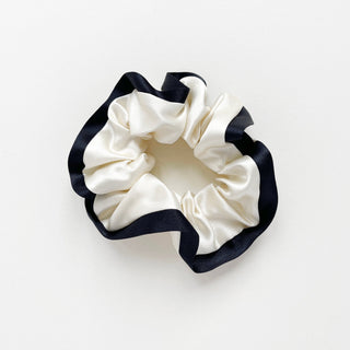 Luxurious white silk scrunchie with contrasting navy blue edge trim, showcasing the ruffled texture and elegant sheen of 100% silk material