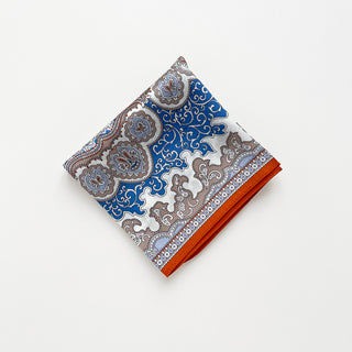 Folded silk scarf with blue and orange baroque pattern, featuring ornate paisley designs and intricate geometric motifs on white background