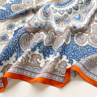 Silk scarf with intricate baroque pattern in blue, orange and beige tones, featuring ornate paisley designs and decorative orange border on luxurious fabric.