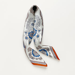 Silk scarf with intricate baroque pattern in blue, orange and beige tones, featuring ornate paisley designs and decorative orange border on luxurious fabric.