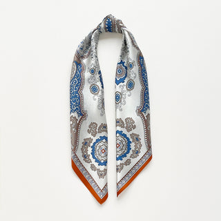 Silk scarf with intricate baroque pattern in blue, orange and beige tones, featuring ornate paisley designs and decorative orange border on luxurious fabric.