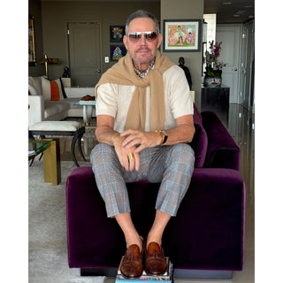 Man wearing a cream knitted polo shirt styled with a geometric print silk neckerchief scarf in warm brown and blue tones.