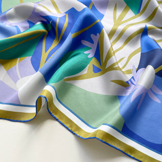 Luxurious silk scarf with abstract lotus pattern in vibrant blues, greens, lilac and mustard yellow, featuring hand-rolled edges and flowing fabric.