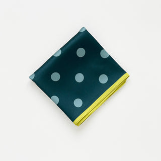 Square silk scarf with teal green background featuring light blue polka dots and vibrant mustard yellow border, folded neatly on white surface