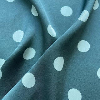 Teal green silk square scarf with light blue polka dots and bright mustard yellow border, elegantly folded showing luxurious sheen and texture