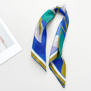 Folded silk scarf featuring abstract lotus design with vibrant blue, teal, mustard yellow, and lilac geometric patterns on white background
