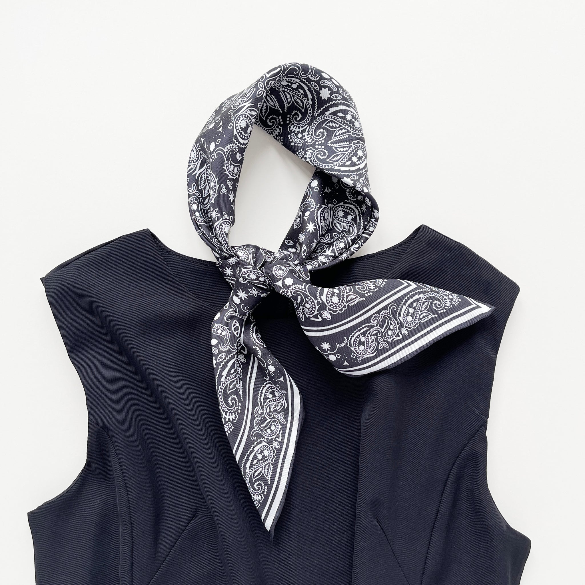 a black and white silk scarf neckerchief featuring bohemian paisley print with hand-rolled edges, knotted as a classic neckerchief, paired with a black dress