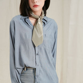 Woman wearing a light blue shirt with a floral patterned silk scarf around their neck against a neutral background