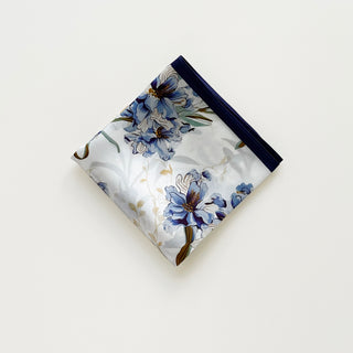 Folded women's silk scarf with blue bell floral pattern on white background, bordered with navy blue edges