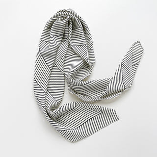 Large black and white women’s silk scarf with geometric stripe pattern and hidden LOVE motif styled in an elegant draped knot.