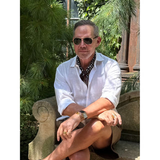 Man wearing a black and white abstract spot silk neckerchief with a white linen shirt and tailored shorts, styled for a timeless smart casual summer look.