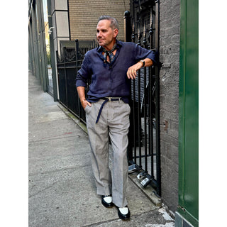 Man wearing a blue patterned silk neckerchief with a navy linen shirt and striped tailored trousers, showcasing timeless men's smart casual style.