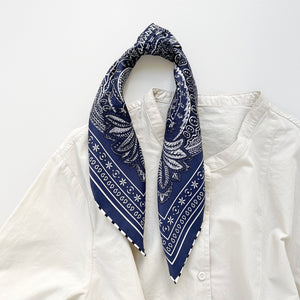 a navy blue silk bandana scarf featuring white and black symmetric pattern with striped hand-rolled edges, knotted as a ponytail head scarf, paired with a light beige turtle neck shirt