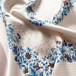 Blush pink silk scarf with elegant blue and burgundy floral leaf pattern border, showcasing lustrous fabric texture and delicate design details.