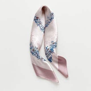 Blush pink silk scarf with elegant blue and burgundy floral leaf pattern border, showcasing lustrous fabric texture and delicate design details.