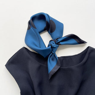 Yale blue silk neckerchief with large black polka dots tied elegantly around the collar of a navy dress, showcasing the scarf's lustrous finish