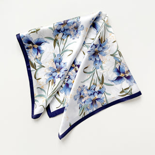 Square silk scarf with blue bell floral pattern on white background, navy blue border trim, elegantly folded to display delicate botanical design
