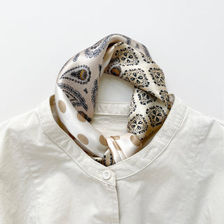 Beige silk bandana scarf with mixed paisley and polka dot patterns in earth tones, styled around the collar of a white shirt