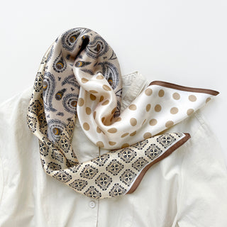 Beige silk bandana scarf with mixed patterns featuring paisley, polka dots, and geometric designs in earth tones, draped over a white shirt