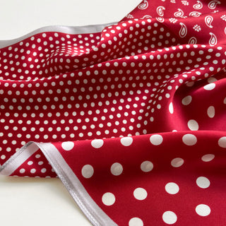 Red silk scarf with white polka dots and paisley pattern, featuring luxurious sheen and silver trim edge, displayed in elegant folds