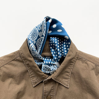 Blue silk bandana with white paisley and polka dot patterns styled as a neckerchief with a beige button-up shirt