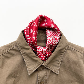 Red silk neckerchief with white paisley and polka dot patterns styled inside the collar of a beige button-up shirt