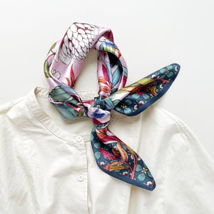 a pink base silk scarf featuring botanic floral print, knotted as a neck scarf, paired with a light beige turtle neck shirt