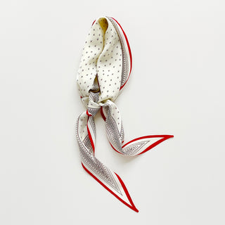 A cream white silk scarf with geometric pattern and a red border tied elegantly with a knot.