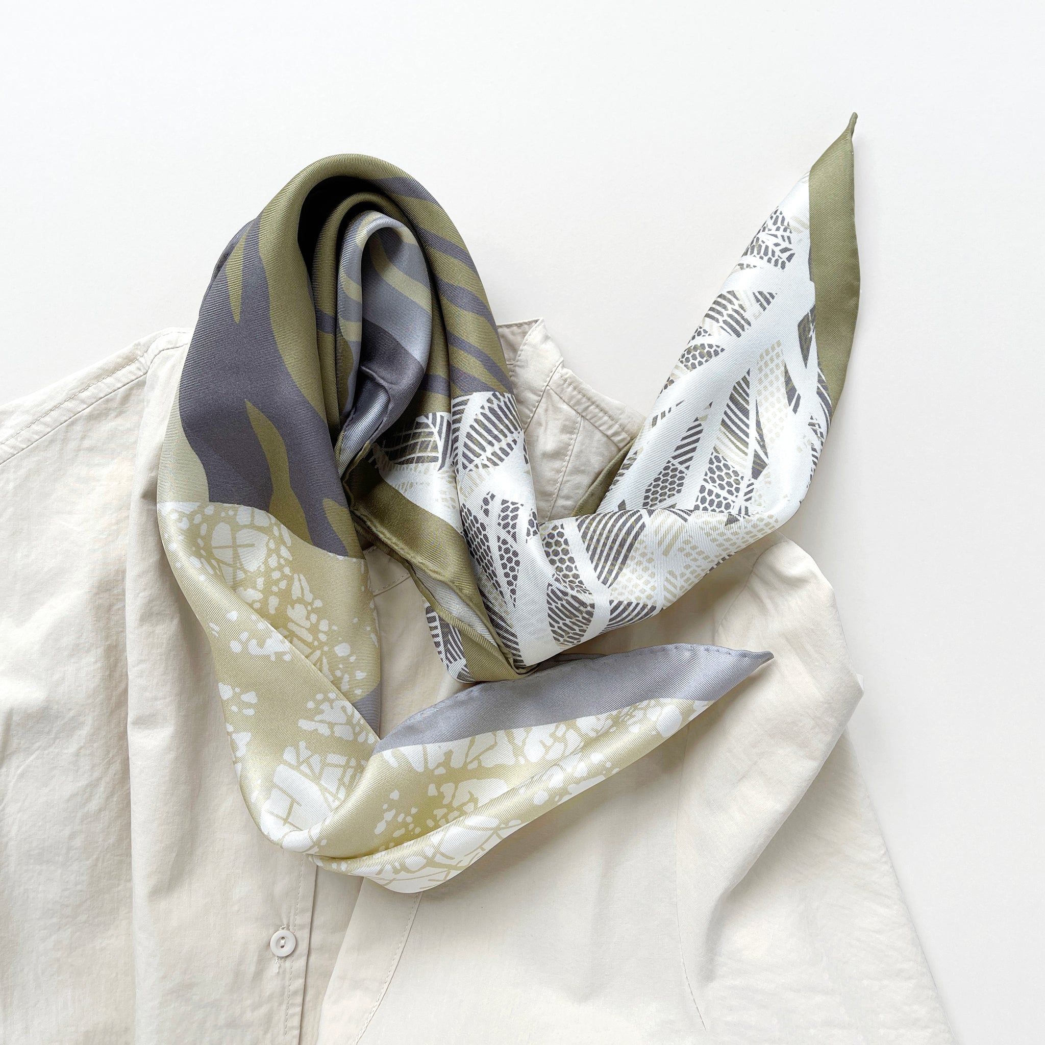 a forest leafy printed square silk scarf in sage green, grey and white tones with hand-rolled edges, paired with a light beige women's shirt