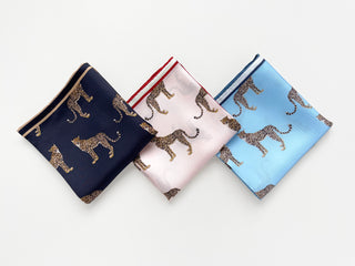 Three silk square scarves with leopard print pattern in black, pink, and sky blue colors, featuring hand-rolled edges and decorative border trim.