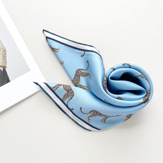 Sky blue silk scarf featuring leopard print pattern with navy and white border trim, elegantly draped to showcase the luxurious fabric and hand-rolled edges.