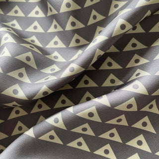 Close-up of charcoal grey silk twill with a pale sage green modernist triangle-and-dot print.