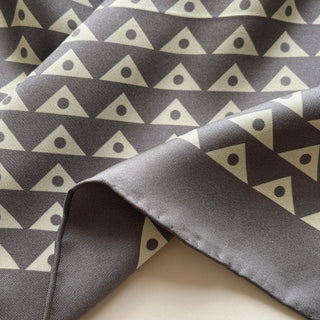 Close-up of charcoal grey silk twill with a pale sage green modernist triangle-and-dot print finished with hand-rolled edges.
